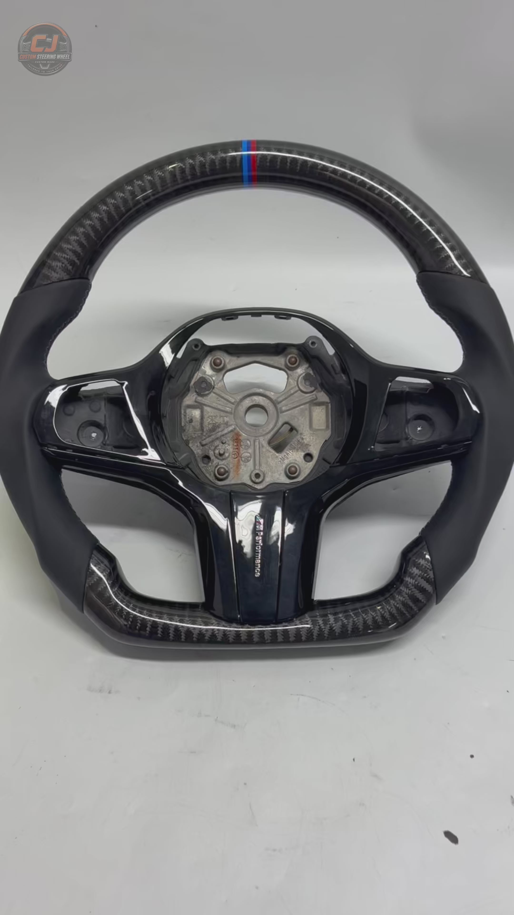 White background product showcase video of CJ Mod Garage BMW custom carbon fiber steering wheel with gloss forged carbon fiber finish, black leather sport grips, gloss black center trim, M tricolor center marker, flat-bottom performance design, and OEM-style fitment for BMW G02 G05 G06 G09 G11 G12 G15 G20 G22 G28 G29 G30 G38 G80 G82 F40 F90