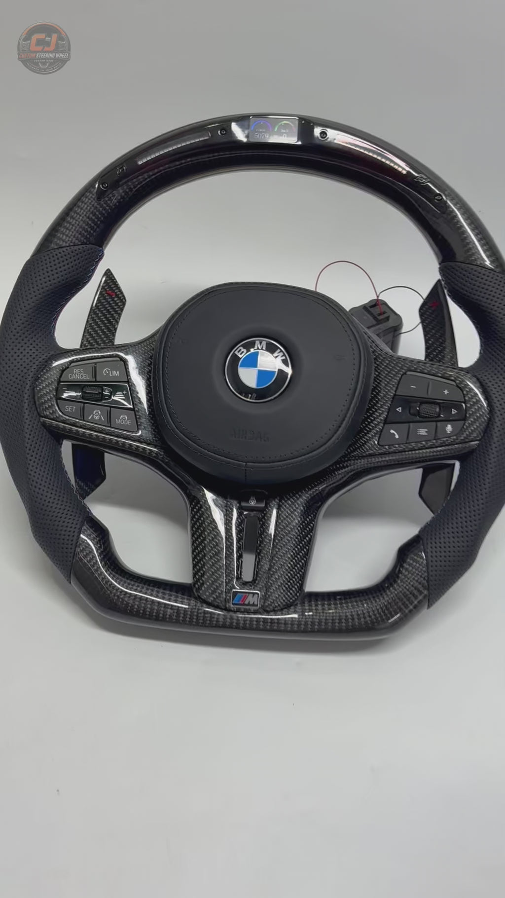 White background product video showing a BMW custom LED carbon fiber steering wheel with digital display, carbon paddle shifters and perforated leather grips compatible with BMW G02 G05 G06 G09 G11 G12 G15 G20 G22 G28 G29 G30 G38 G80 G82 F40 F90 models by CJ Mod Garage