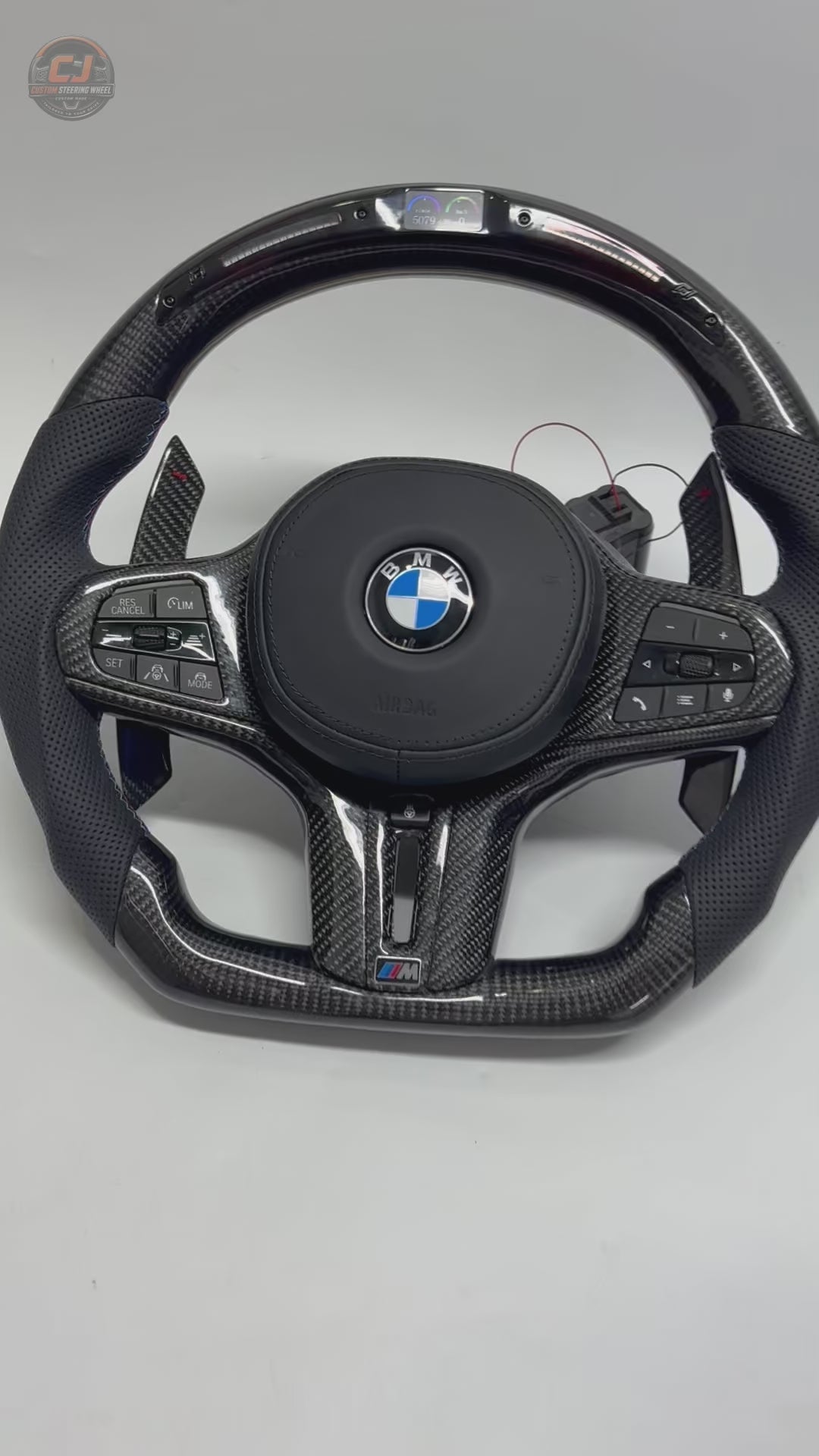 White background product video showing a BMW custom LED carbon fiber steering wheel with digital display, carbon paddle shifters and perforated leather grips compatible with BMW G02 G05 G06 G09 G11 G12 G15 G20 G22 G28 G29 G30 G38 G80 G82 F40 F90 models by CJ Mod Garage
