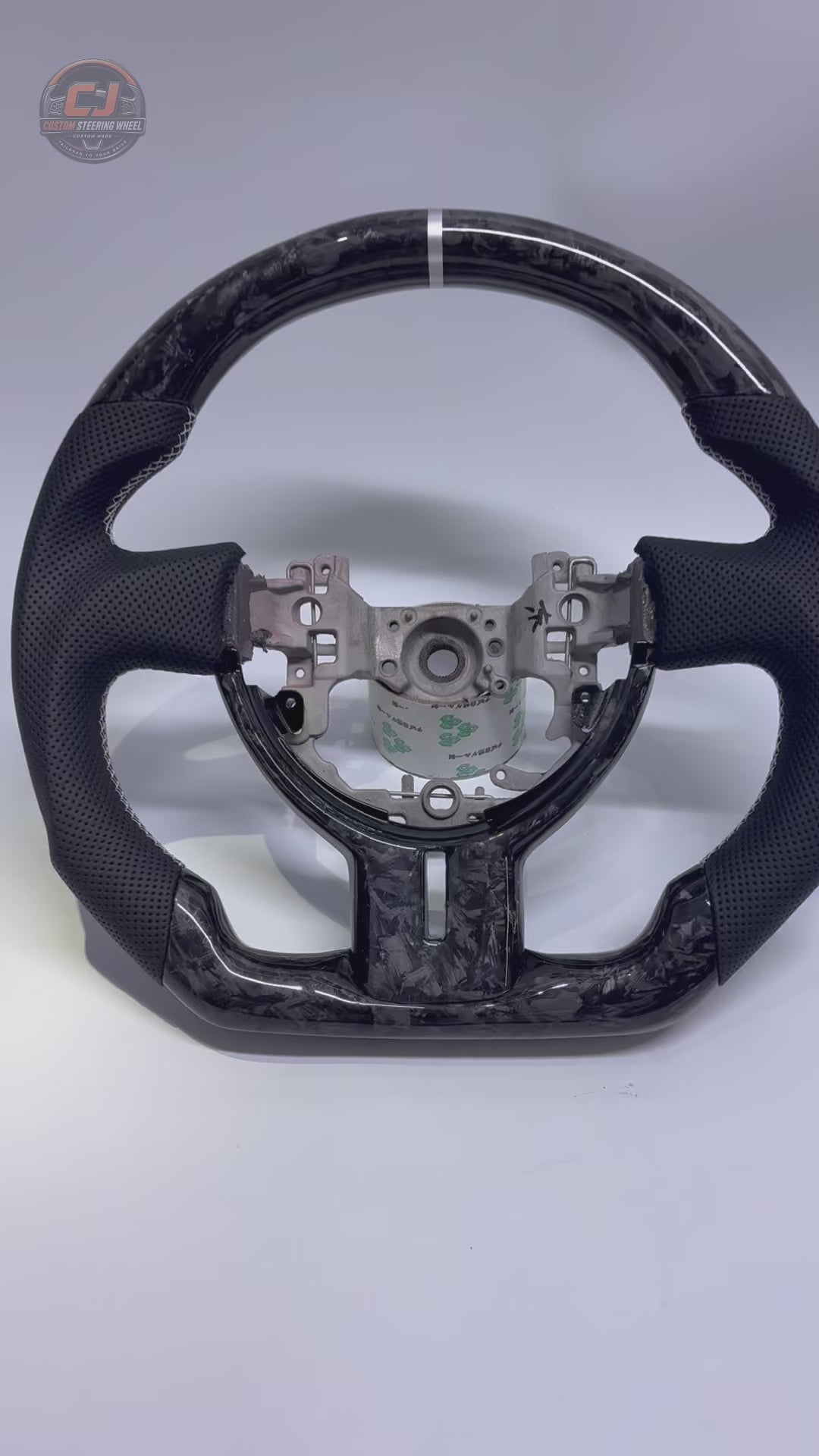 Studio showcase video of Toyota GT86 forged carbon fiber steering wheel with gray flake pattern, perforated leather grips, white stitching and flat-bottom motorsport styling by CJ Mod Garage