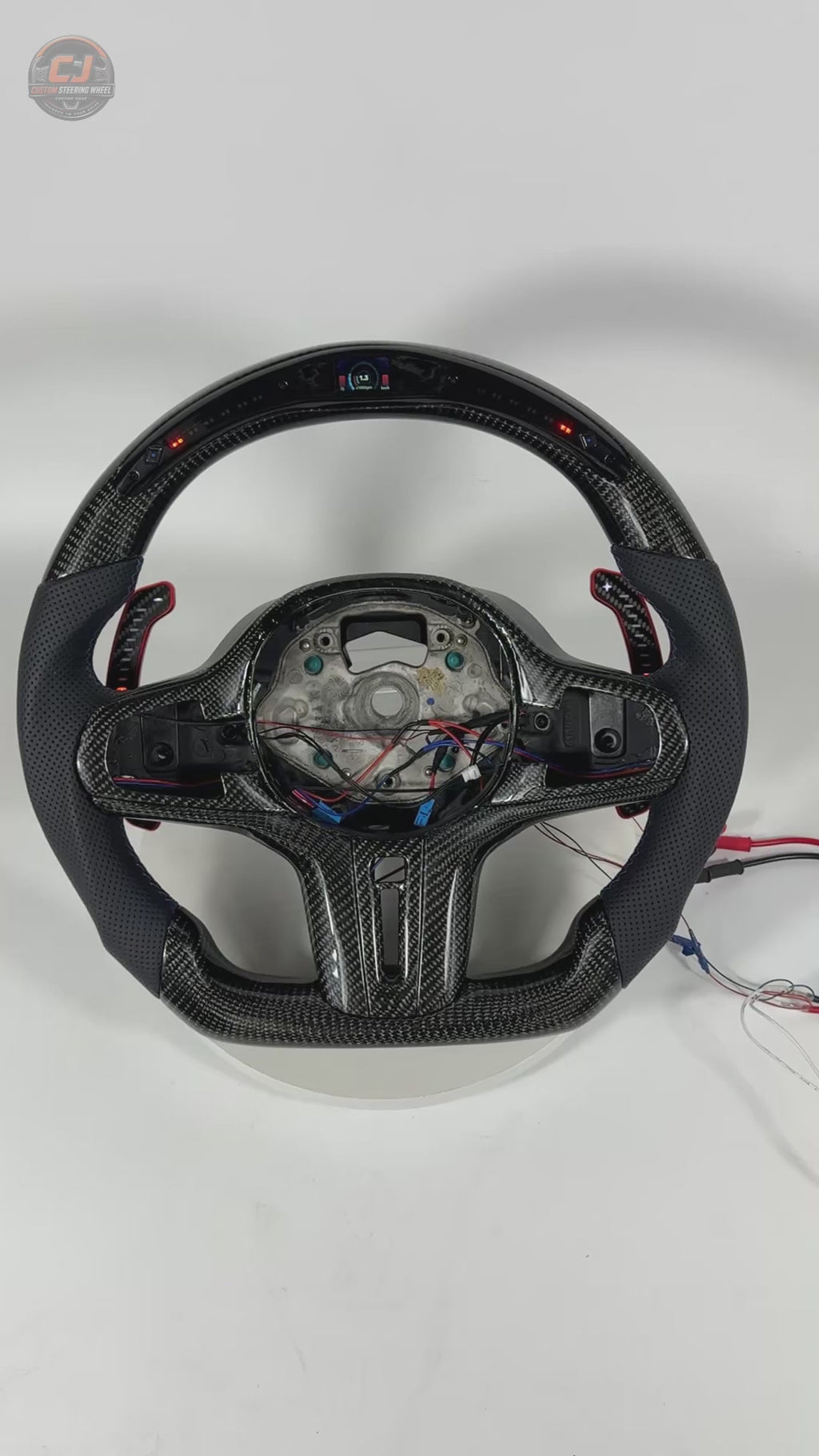 White studio video showcasing BMW custom carbon steering wheel with LED shift lights, perforated leather grips and digital display for BMW G02 G05 G06 G09 G11 G12 G15 G20 G22 G28 G29 G30 G38 G80 G82 F40 F90 by CJ Mod Garage
